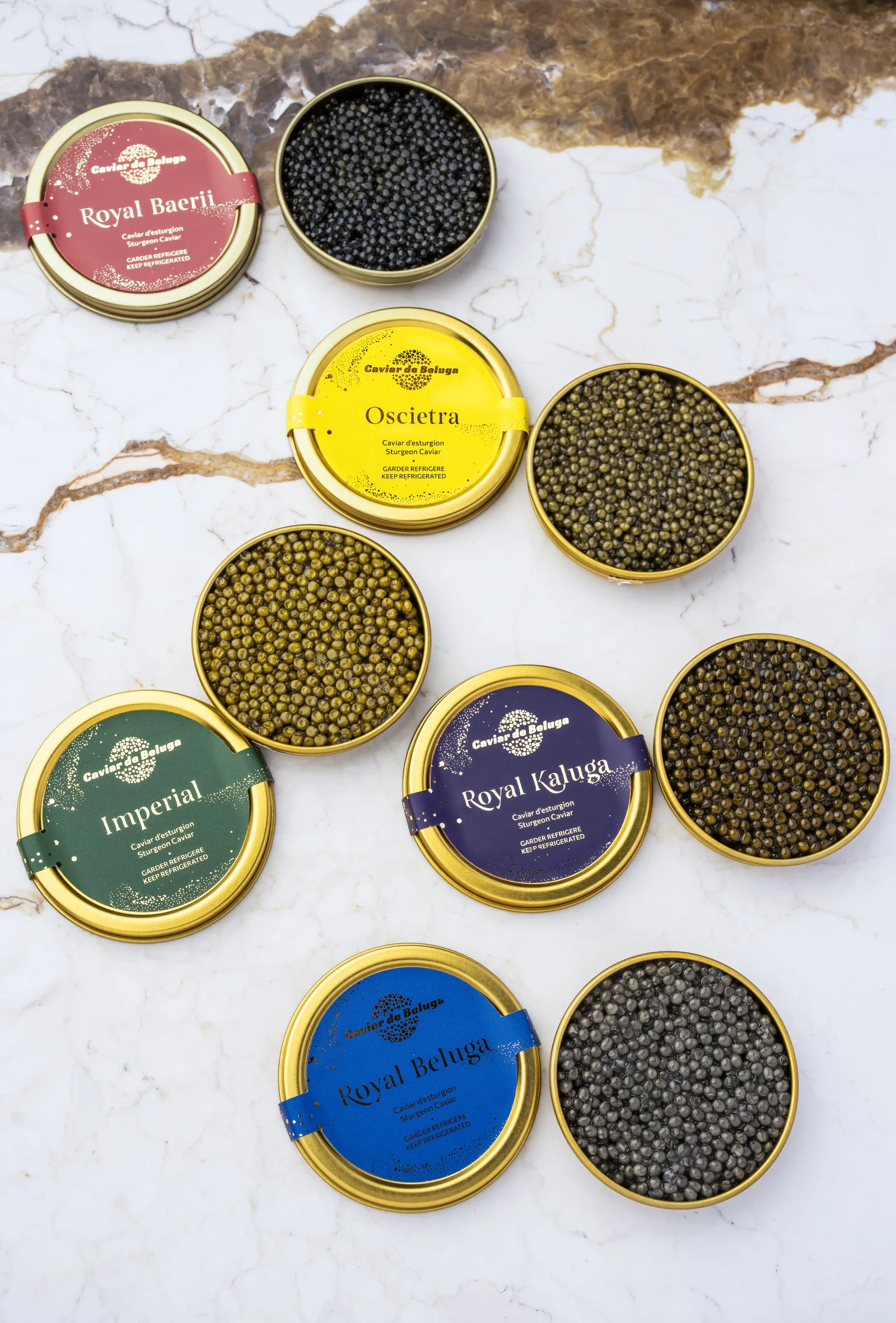 The five Caviar de Beluga tins, each in its own colour, beside their open caviar on marble